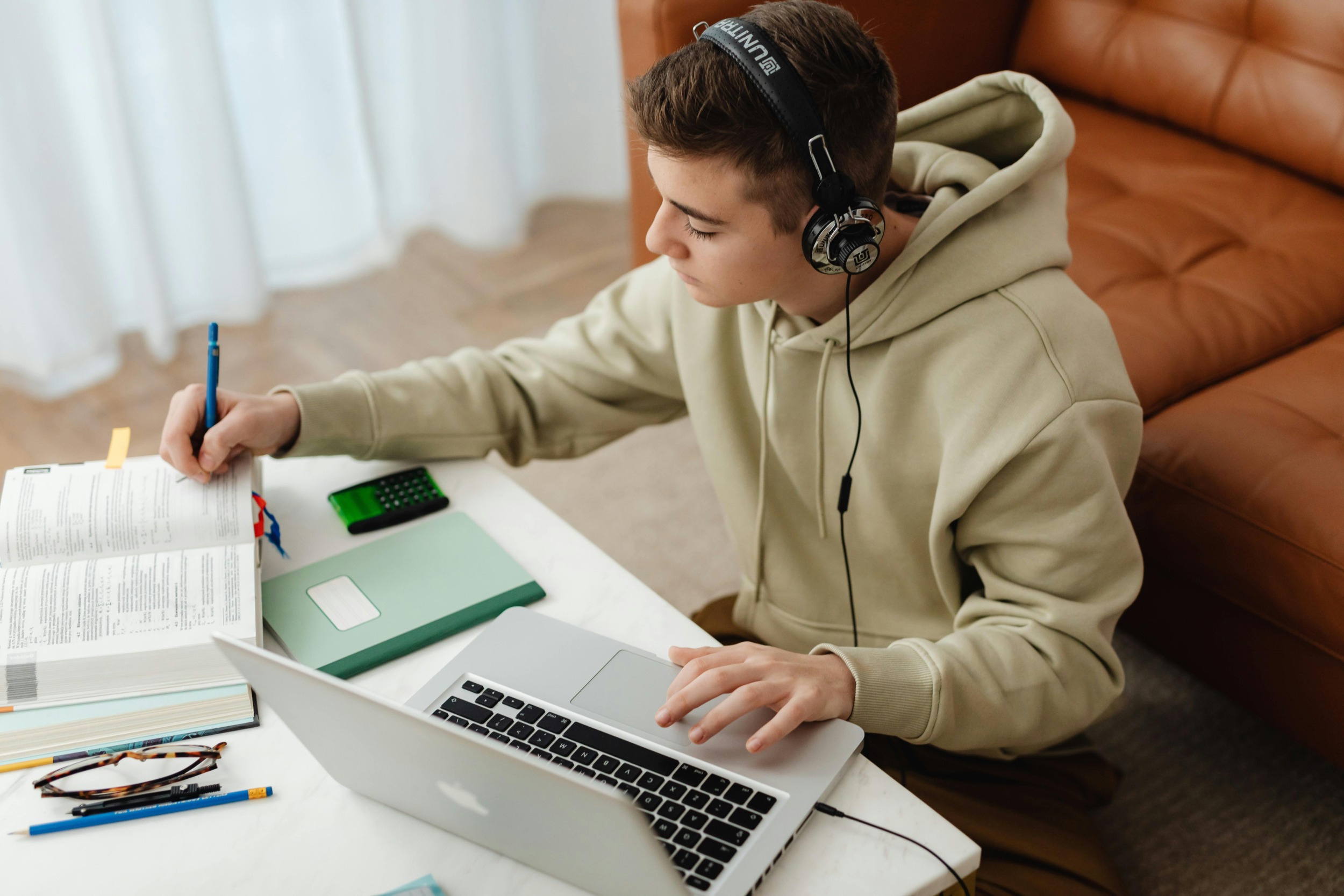 Teachers, schools & ICE raids:Teen boy sits at desk with laptop, headphones and open books.