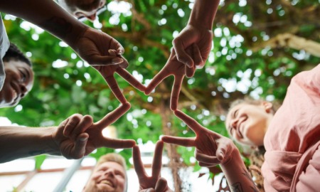 Youthsystems and communities: Five people (aults ad children) stand facing each other in a circle, touching their fingers together to for a star