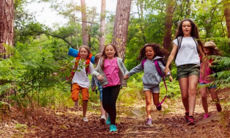 Nature of Outdoors_stronger youth development through exploration report, youth in nature: Boys and girls running in the forest together holding hands on a trail during school nature camping trip