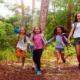 Nature of Outdoors_stronger youth development through exploration report, youth in nature: Boys and girls running in the forest together holding hands on a trail during school nature camping trip