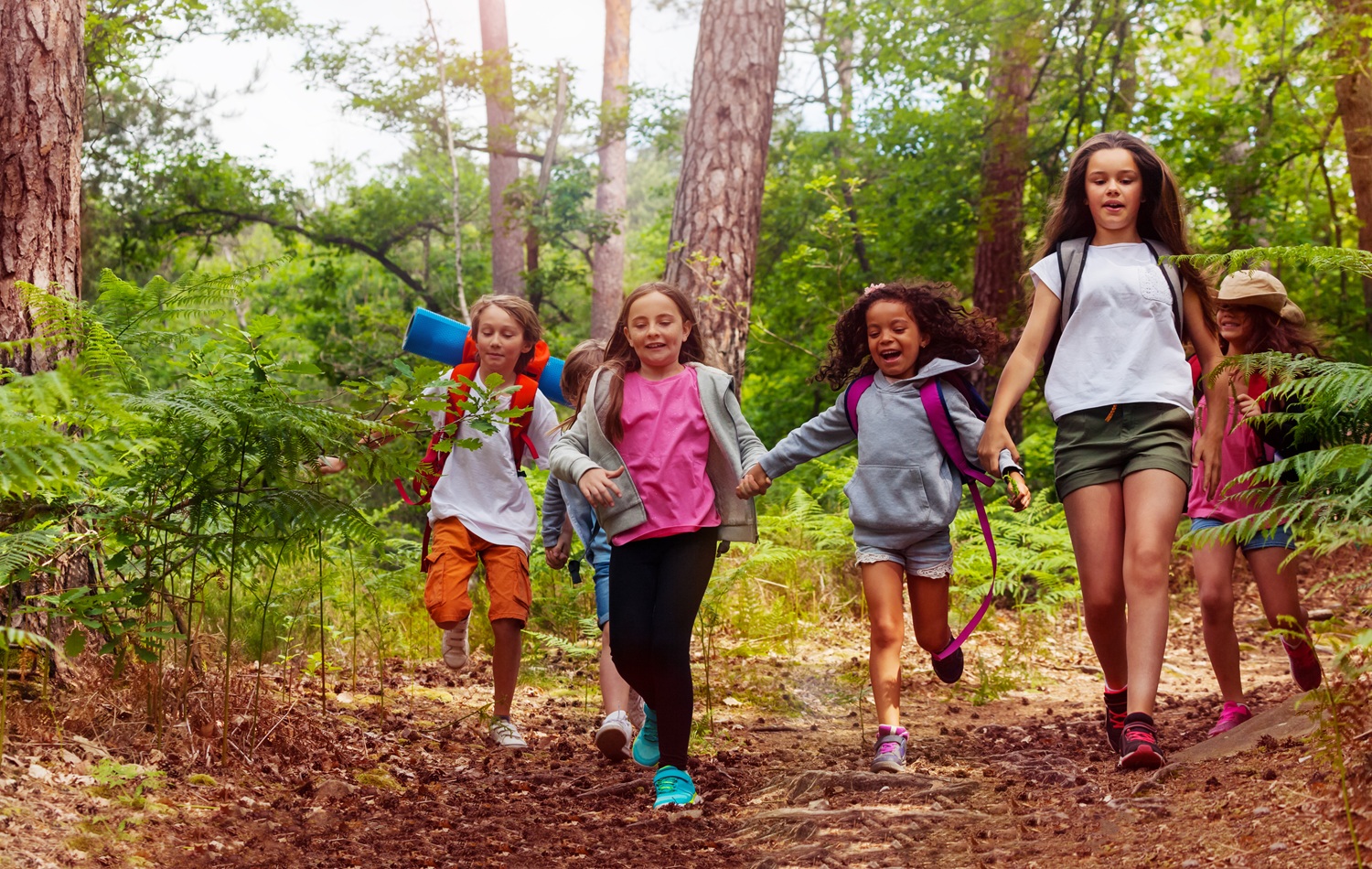 Nature of Outdoors_stronger youth development through exploration report, youth in nature: Boys and girls running in the forest together holding hands on a trail during school nature camping trip