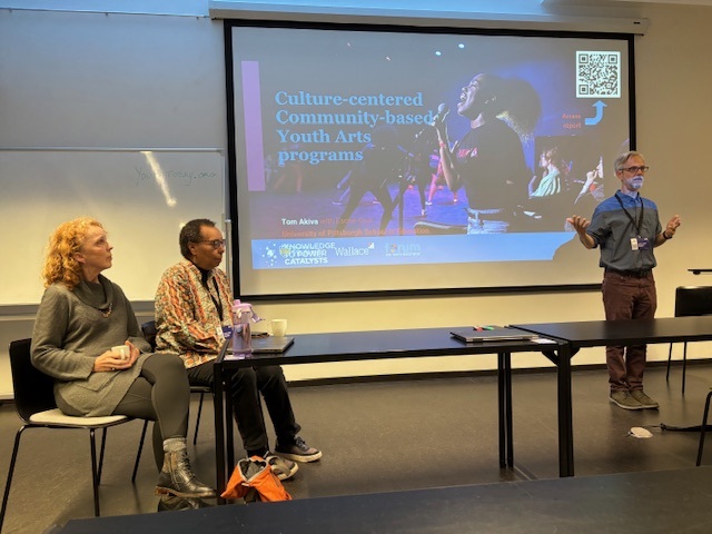 New opportunities to explore extended learning and youth development across the globe: man stands and presents a projected presentation while other look on