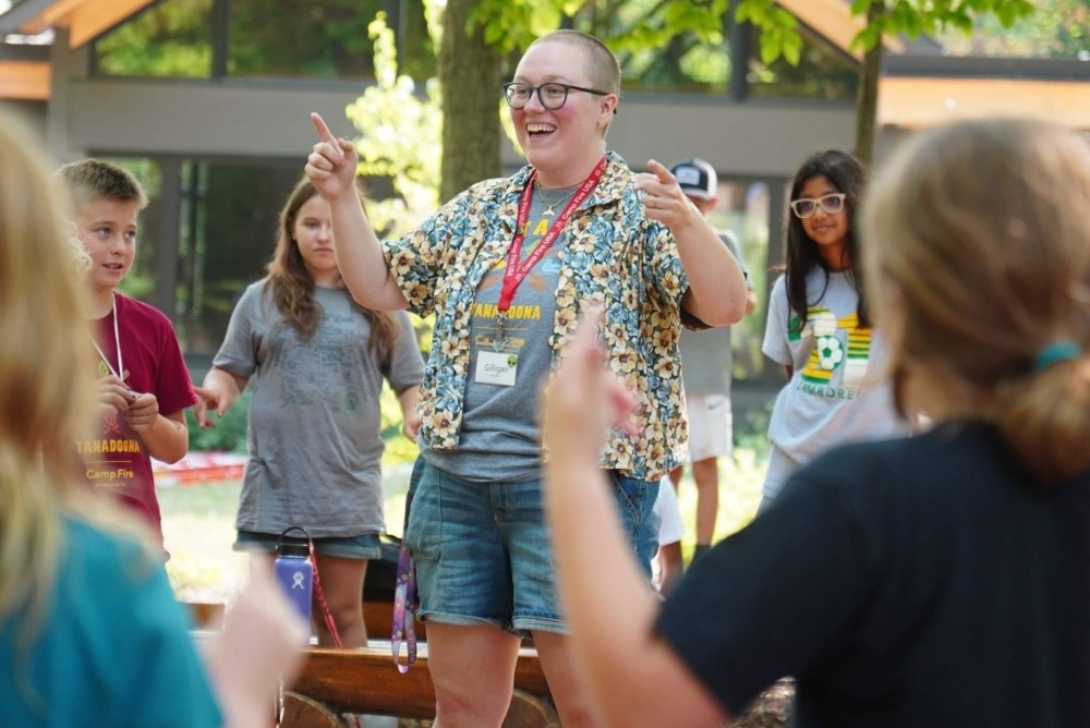 Camp Fire LGBTQ & Trans inclusion: Adult leads activity with group of campers standing around them in a circle
