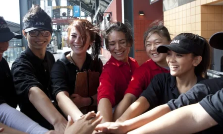 JUMA VENTURES:Group of young people stand close together istacking hands in center of circle