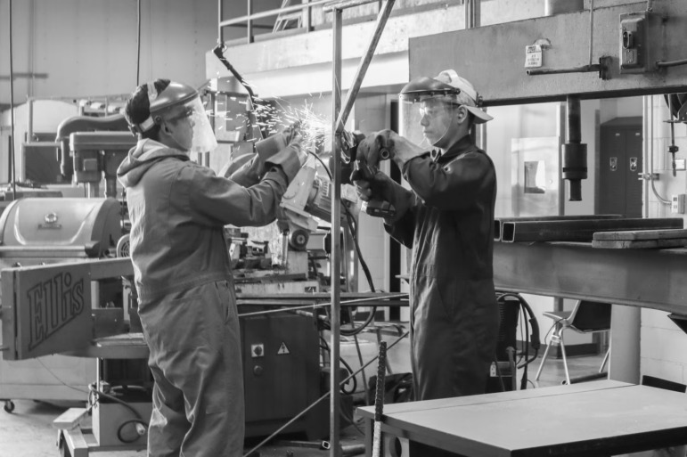 High school diploma pathways: Two people in metal welding masks stand opposite each other using welding torches to fabricate metal