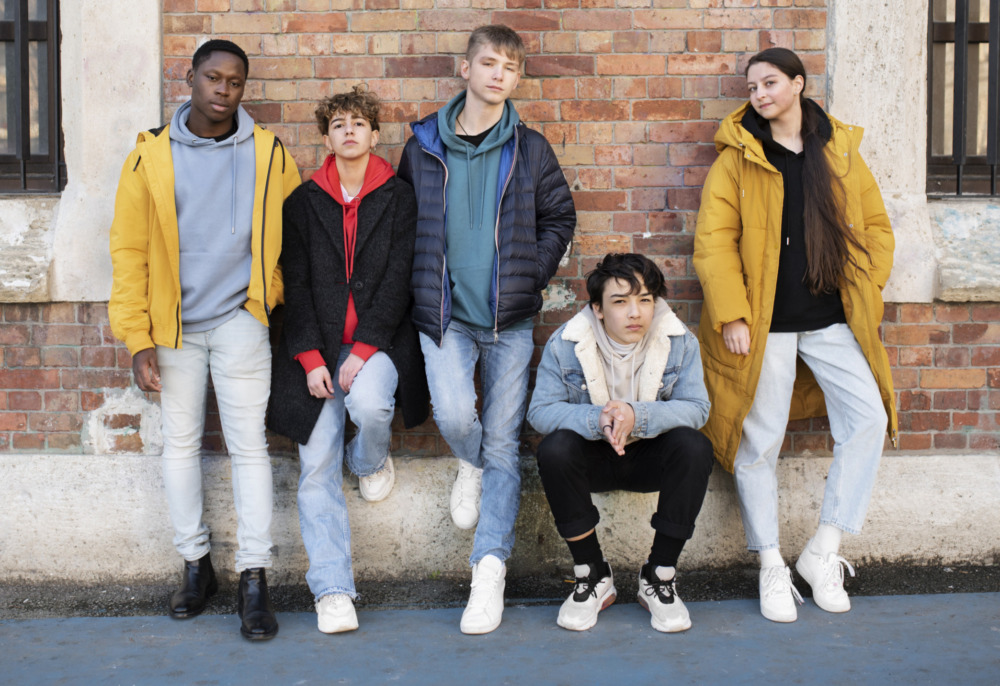 Student reengagement: Five mult-ethnic teens in winter jackets stand in front of brick wall
