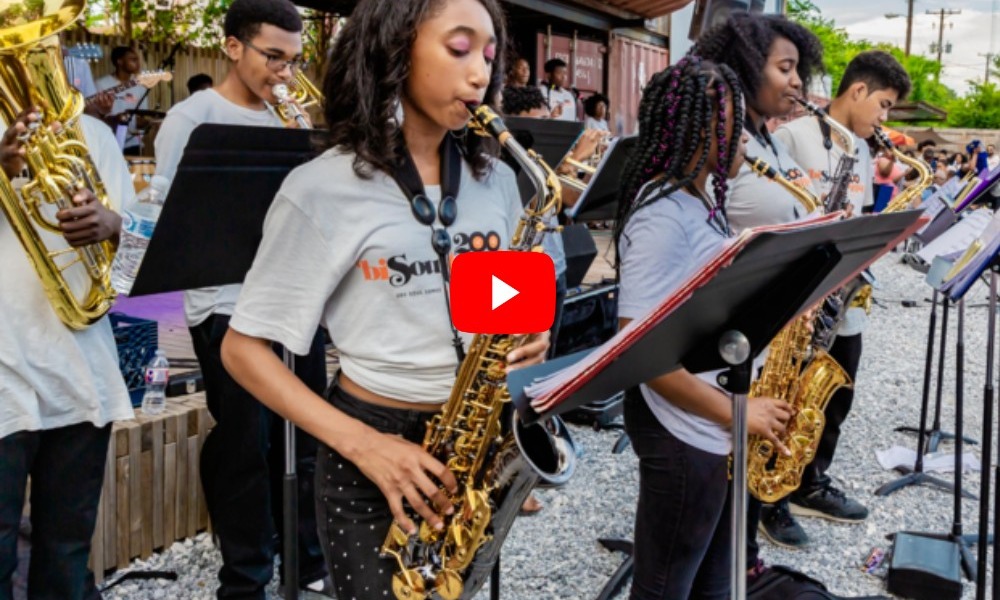 Youth band playing outdoor concert with closeup on wins section standing at front of stage