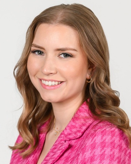 Paige Swanstein headshot: white woman with long hair in pink checker blazer