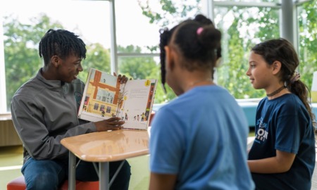 QA how service learning, done well, changes lives: black male youth reads a book to younger girls and shows them pictures