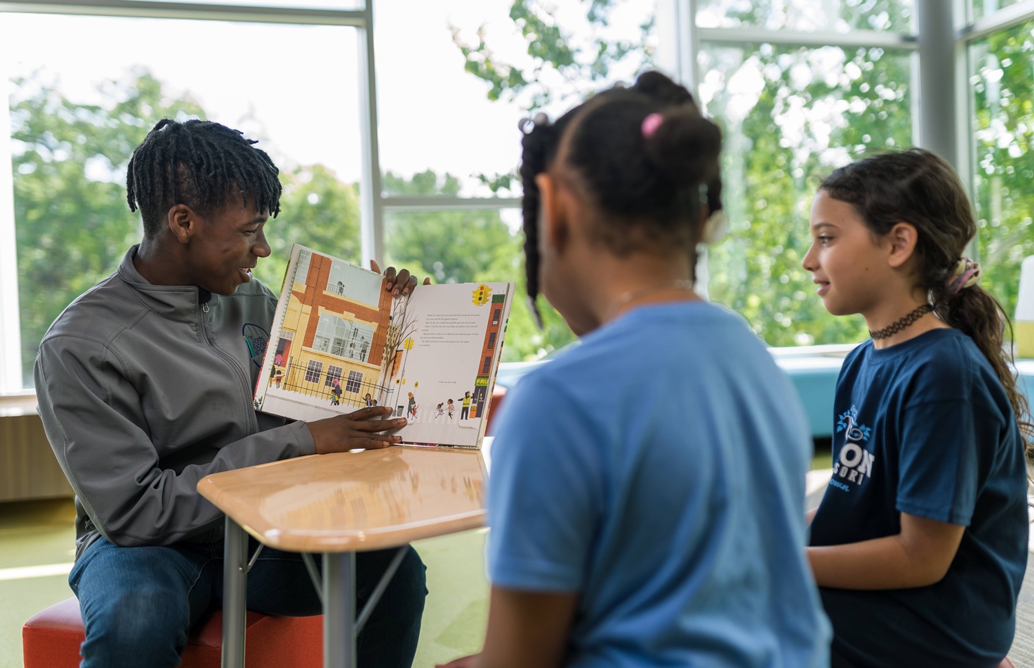 QA how service learning, done well, changes lives: black male youth reads a book to younger girls and shows them pictures