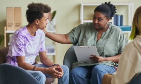 Youth mental health is personal_Our solutions need to be systemic: black female therapist comforts black male student during therapy