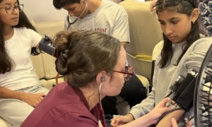 Missing conversation_heart disease and teen years_feature: two young female students getting their blood pressure taken at health event