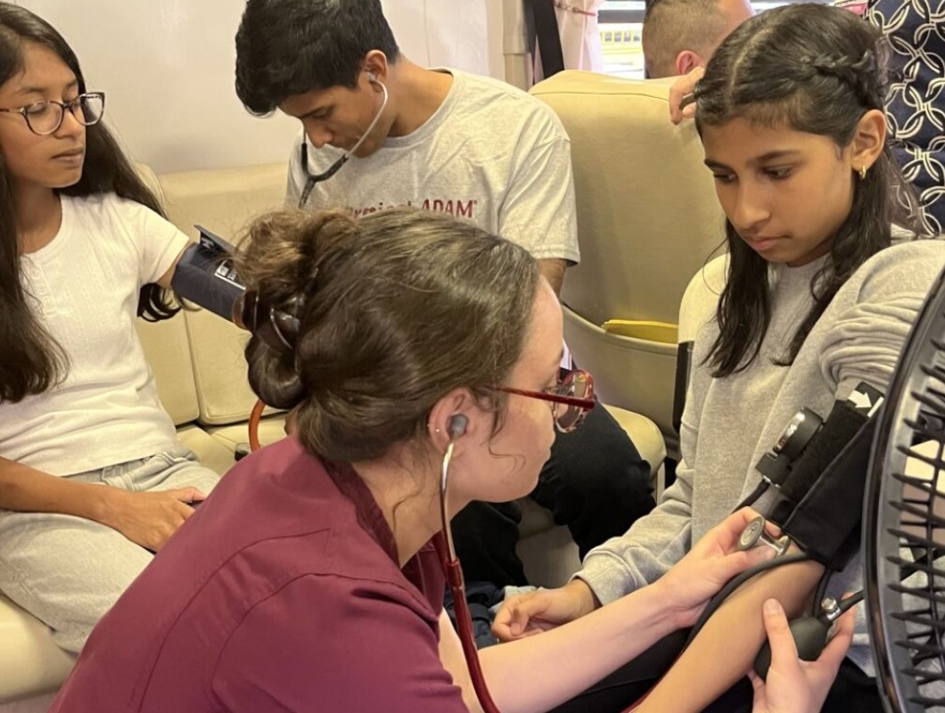 Missing conversation_heart disease and teen years_feature: two young female students getting their blood pressure taken at health event