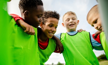 Reimagining youth sport_putting positive youth development first: group of young boys in green training bibs huddled together smiling and talking