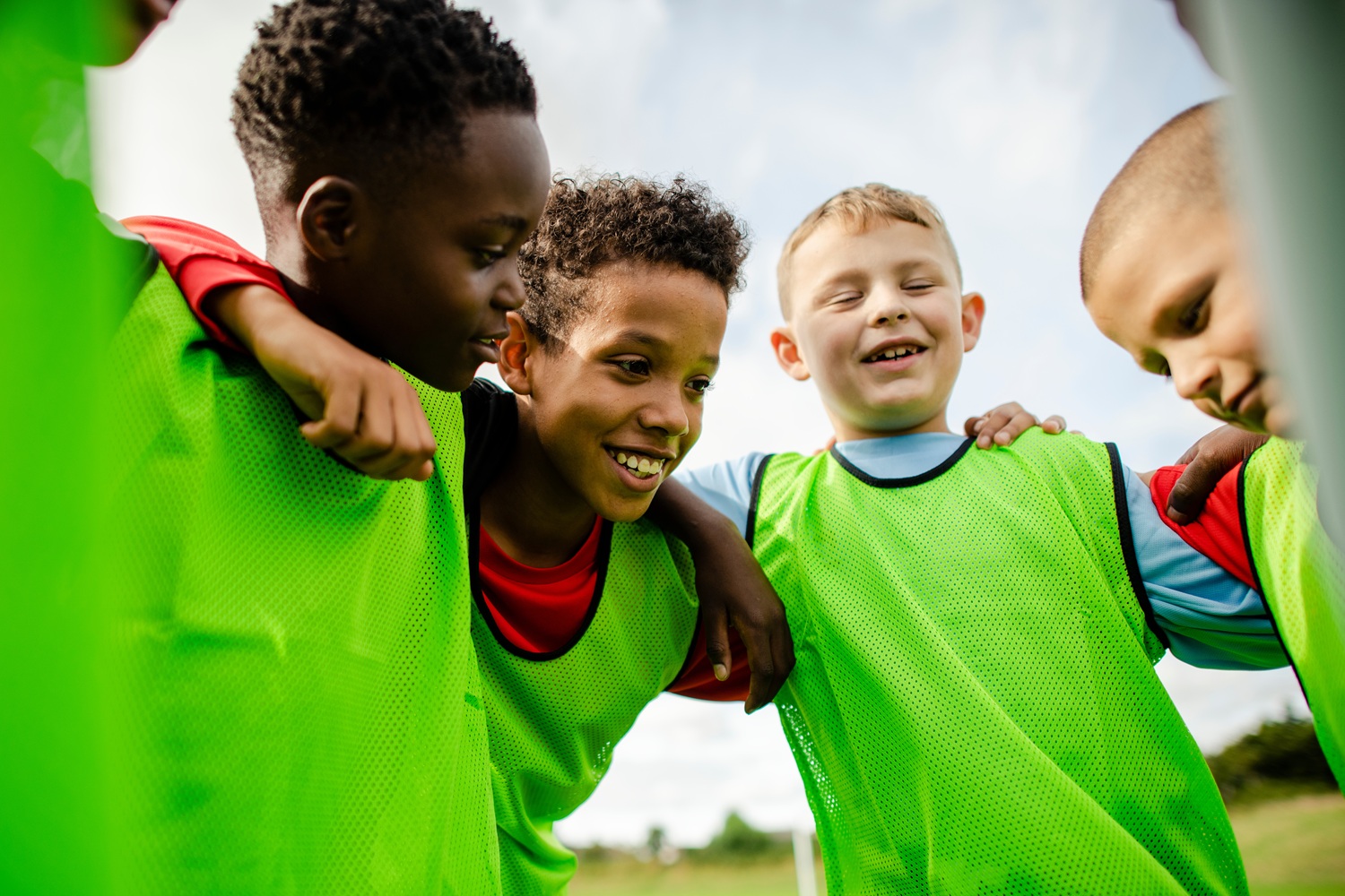 Reimagining youth sport_putting positive youth development first: group of young boys in green training bibs huddled together smiling and talking