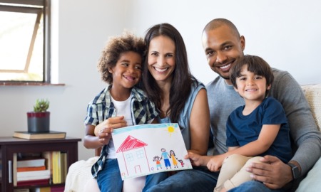 Sieze the foster care insurance crisis as an opportunity to curb foster care: happy interracial family smiling and holding child's drawing of home and family