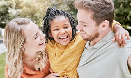 Adoption and adoptive family support grants: white couple smiling and holding happy black child outdoors