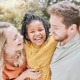 Adoption and adoptive family support grants: white couple smiling and holding happy black child outdoors