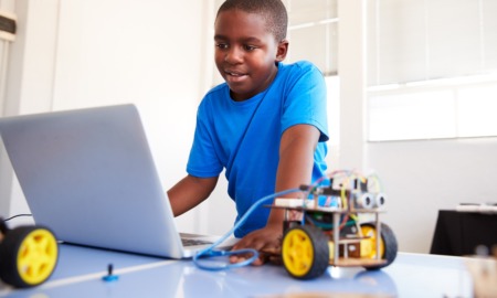 Afterschool STEM education: young black boy working on laptop connected to robotic wheel device