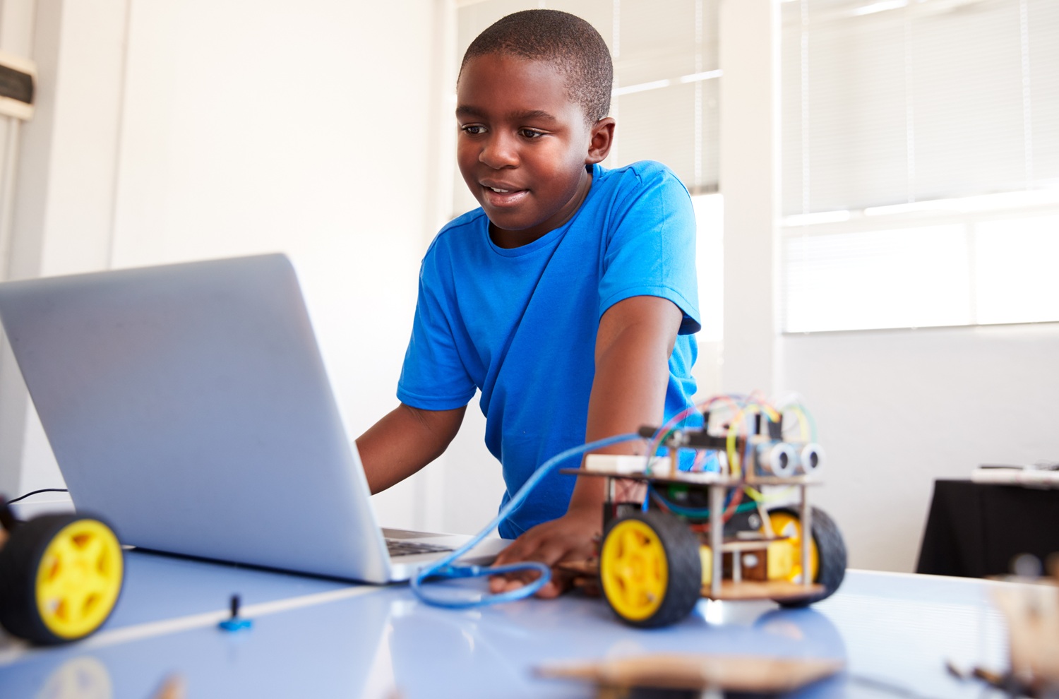 Afterschool STEM education: young black boy working on laptop connected to robotic wheel device