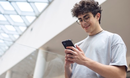 Beyond Balance_how digital platforms can intentionally foster teen emotional development: happy male teenager with dark hair and glasses looking down at phone