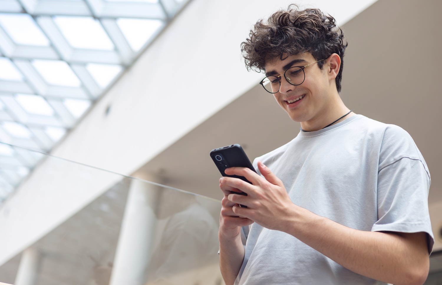 Beyond Balance_how digital platforms can intentionally foster teen emotional development: happy male teenager with dark hair and glasses looking down at phone
