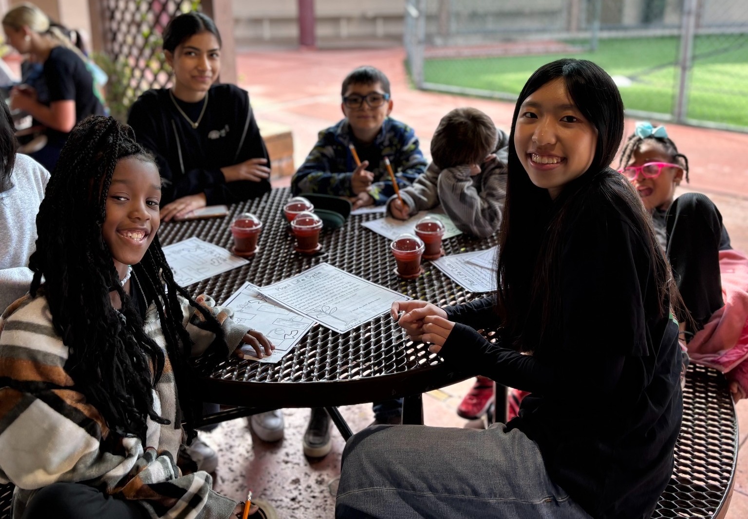 Expanding horizons, essential developmental relationships _evidence of afterschool impacts_feature: group of students and afterschool workers at a table outdoors doing work