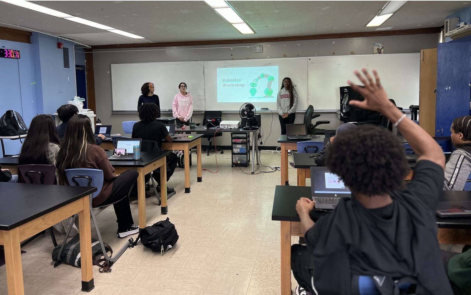What happens when Bronx students lead the way in STEM equity_hand raise: view from back of classroom of student raising hand to ask question while a robotics workshop presentation is happening