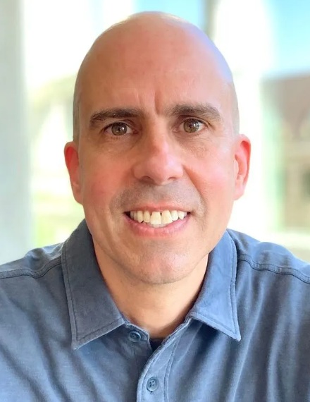 Dan Gonzelez headshot: white bald man in denim button-up shirt smiling