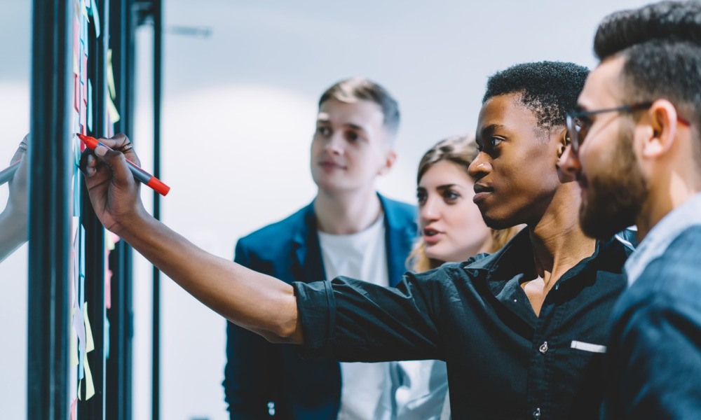 From developmental relationships to opportunities_social capital mobilization_feature: black male youth confidently writes on idea wall in front of peers