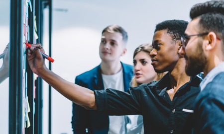 From developmental relationships to opportunities_social capital mobilization_feature: black male youth confidently writes on idea wall in front of peers