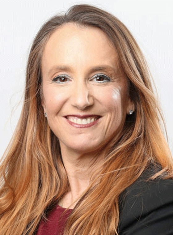 صورة جودي غرانت: امرأة بيضاء ذات شعر أشقر طويل تبتسم أمام خلفية بيضاء