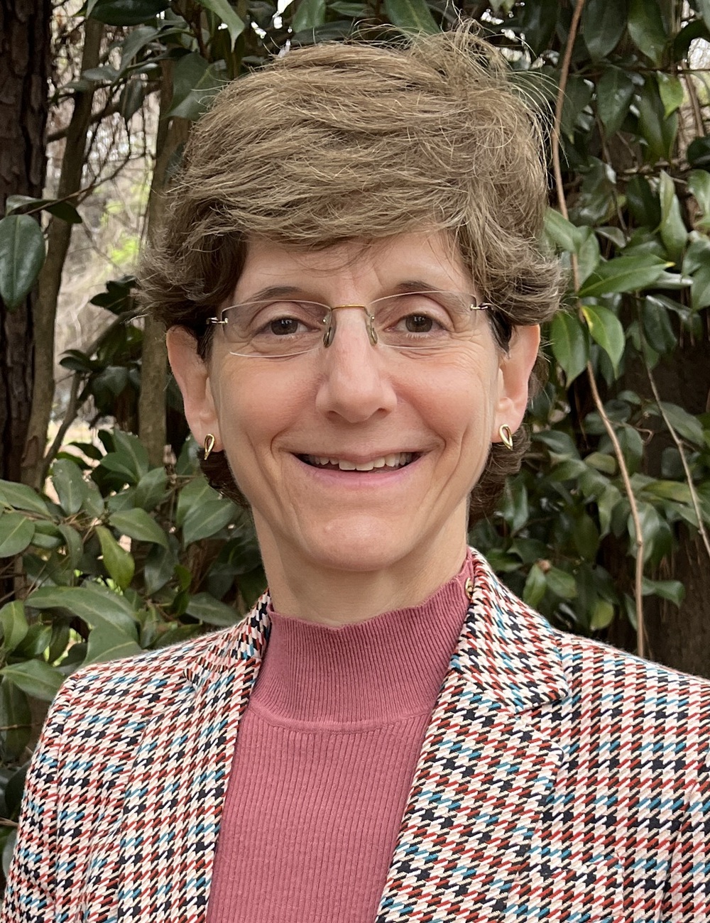 صورة ليزا أمان: امرأة بيضاء كبيرة السن ذات شعر بني قصير وترتدي نظارات في الهواء الطلق