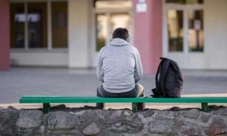 What back to school season reveals about foster youth, attendance crisis: male student sits outside school alone with backpack on bench beside him