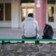 What back to school season reveals about foster youth, attendance crisis: male student sits outside school alone with backpack on bench beside him