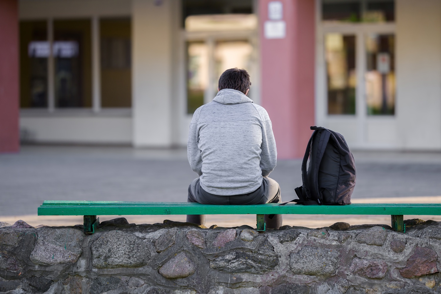 What back to school season reveals about foster youth, attendance crisis: male student sits outside school alone with backpack on bench beside him