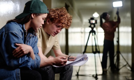 Mid-Atlantic young filmmaker project support grants: Two young individuals sitting together and reviewing script in a film production setting with a tripod and lighting equipment in background