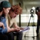 Mid-Atlantic young filmmaker project support grants: Two young individuals sitting together and reviewing script in a film production setting with a tripod and lighting equipment in background