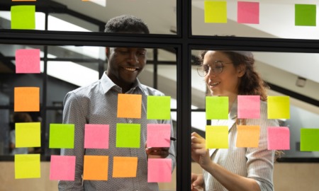 Q&A_Alex Lohrbach_Elevating Youth Engagement curriculum_ youth-adult partnership feature: two people work together on glass wall of post it notes