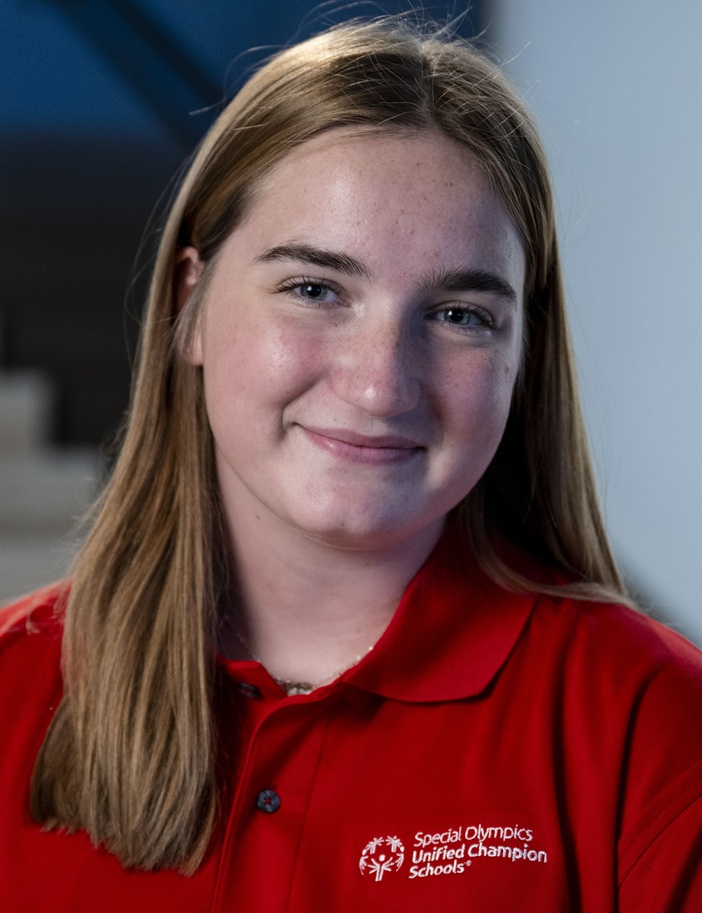 Skylar Spencer headshot: young white woman in red collared shirt and long brown hair smiling
