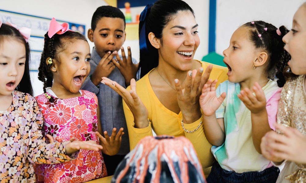 College students can help close the gap between demand and availability for afterschool programs_feature: young woman with group of excited young children around model volcano in afterschool program