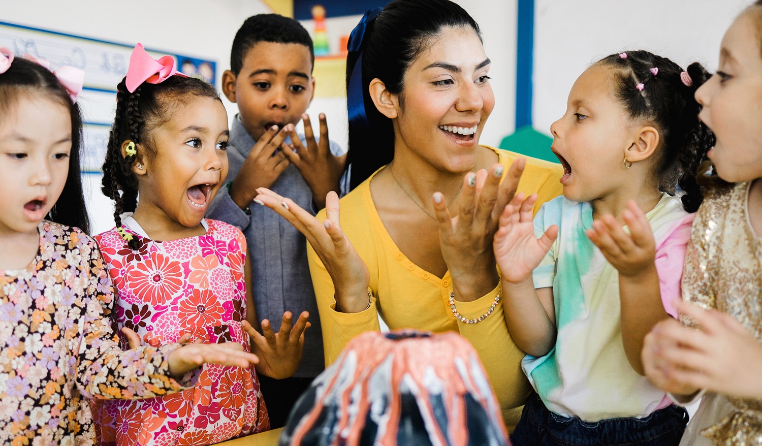 College students can help close the gap between demand and availability for afterschool programs_feature: young woman with group of excited young children around model volcano in afterschool program