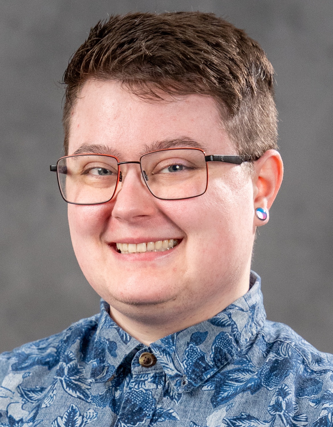 Lorant Peeler headshot: young white person in glasses and blue patterned button up shirt