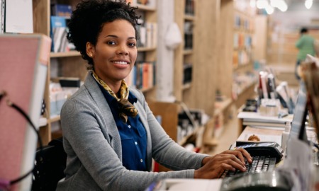 Library support, professional and workforce development program grants: happy young black woman at library desk smiling