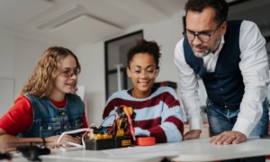 Coaching not correction_The shift youth serving systems need to build real leaders_feature: male educator/mentor helping two girls with STEM project