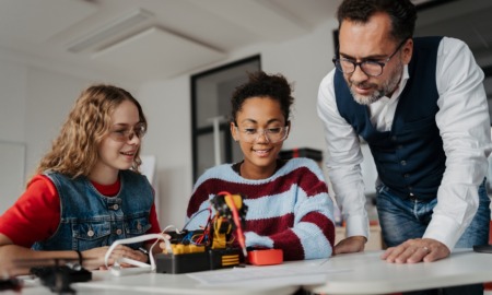 Coaching not correction_The shift youth serving systems need to build real leaders_feature: male educator/mentor helping two girls with STEM project