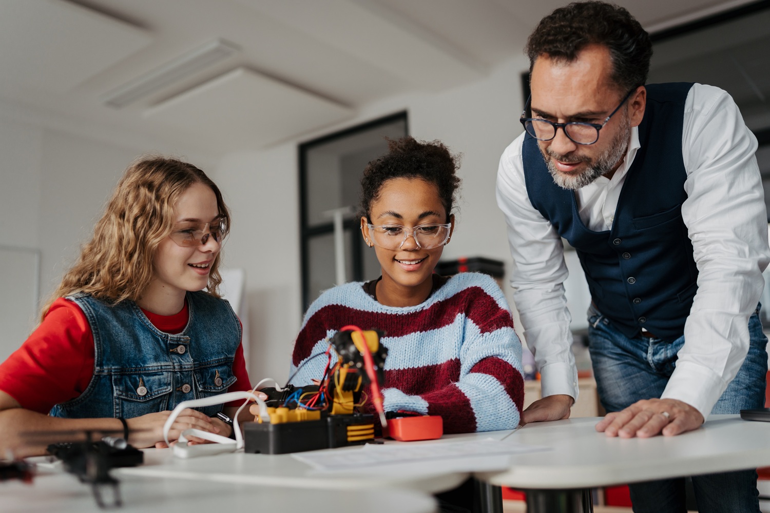 Coaching not correction_The shift youth serving systems need to build real leaders_feature: male educator/mentor helping two girls with STEM project