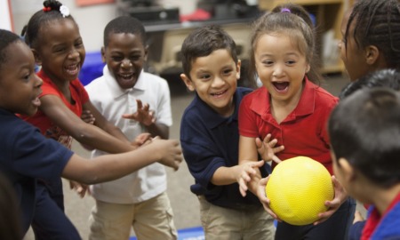 Joy, partnership and play create belonging and increase attendance_feature: recess, group of very happy children playing game with yellow ball