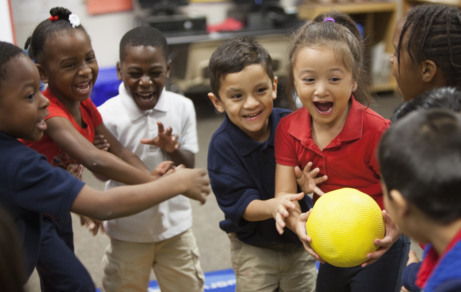 Joy, partnership and play create belonging and increase attendance_feature: recess, group of very happy children playing game with yellow ball