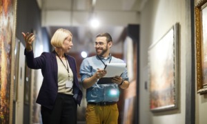 Museum staff professional development and training program grants_feature: Portrait of two cheerful museum workers discussing paintings walking in art gallery, copy space